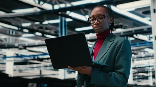 Managing Databases Laptop and Female Technician Walking in Data Center
