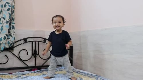 cute toddler baby boy trying to stand for the first time at bed at home