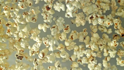 Popcorn fliegt hoch und fällt auf hellem Hintergrund herunter, gefilmt mit einer Hochgeschwindigkeitskamera mit 1000 Bildern pro Sekunde