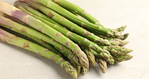 Woman taking fresh raw asparagus at light grey table, closeup