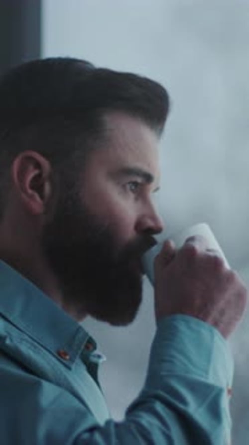 Man Drinks Coffee by Window on a Cloudy Day