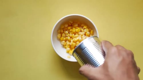Sweetcorn Pouring From a Canned Container on Yellow Background
