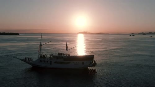 A right to left pan drone shot of a boat in the sea during the sunset with beautiful sun reflection.