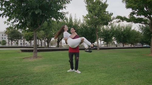 Young Teen Guy Playing with Girlfriend on His Hands in City Green Park