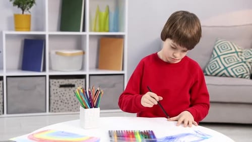 Kleiner Junge zeichnet mit schwarzem Stift am weißen Tisch drinnen