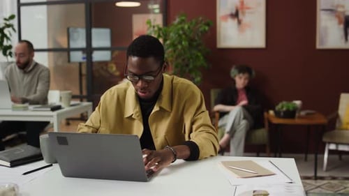 African American Young Man Typing on Laptop at Work Desk in Office