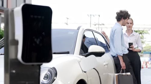 Progressive businessman and businesswoman leaning on EV car and charging point.