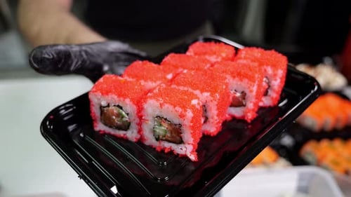 A Closeup Chef in Gloves Holds a Plate of Sushi in the Restaurant's Kitchen