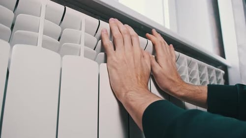 Male Palms Touch a Cold Heating Radiator Against the Wall