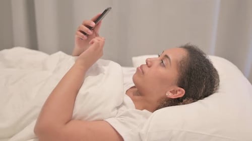 Side View of African American Woman using Smartphone in Bed