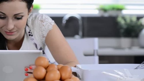 Cheerful brunette woman uses tablet computer while baking cupcakes at home