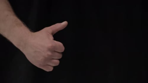 Hand Gives Thumbs Up Gesture on Black Background