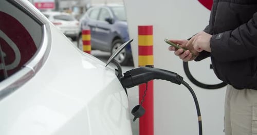 Businessman Charging Electric Car at Outdoor Charging Station Unrecognizable Man Plugging Electric