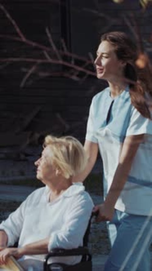 Woman pushing senior in wheelchair outside on sunny day