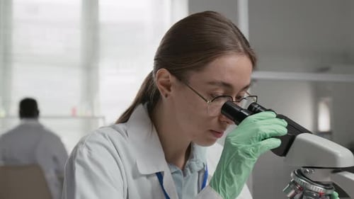 Woman Analyzes Sample Under Microscope in Bright Lab