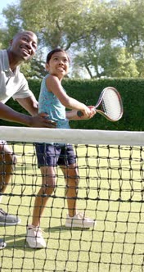 Vertical video: Teaching tennis, father guiding daughter on court, holding racket together