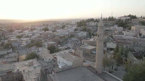 Aerial view of minaret and stone cityscape stretching toward hills in Mardin Turkey