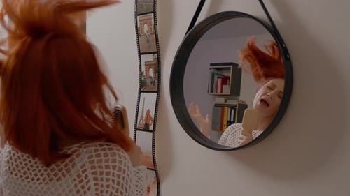 Cheerful woman sings and dances in her bedroom mirror with hair comb