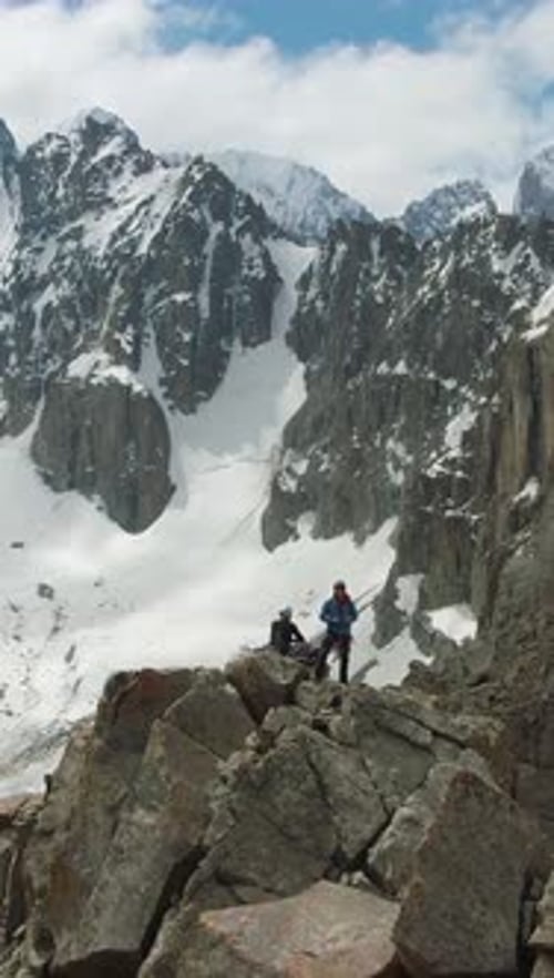 Two Climbers on Peak of Rock SnowCapped Mountains Aerial View Vertical Video