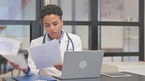 Mixed Race Female Doctor Working on Medical Documents and Laptop