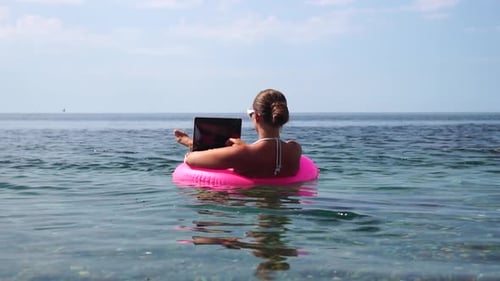 Woman Freelancer Works on Laptop Swimming in Sea on Pink Inflatable Ring Happy Tourist in Sunglasses