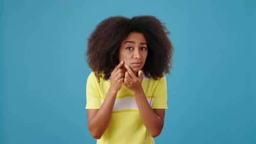 Triste femme afro-américaine avec acné et cheveux secs sur fond bleu