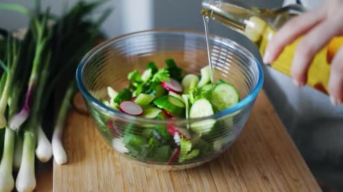 Woman Hands Pouring Olive Oil Into Glass Bowl with Fresh Spring Salad