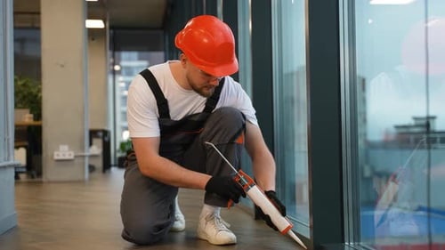 Man Caulking Windows in Modern Office Building
