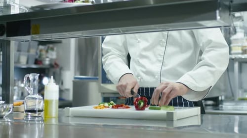Professional chef in a commercial kitchen in a restaurant or hotel is slicing green vegetables.
