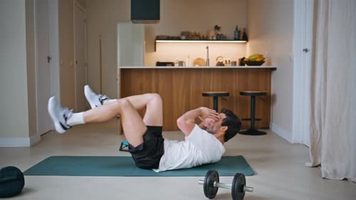 Aktiver Sportler trainiert Bauchmuskeln auf Fitnessmatte für zu Hause, energischer Mann, der die Beine hebt