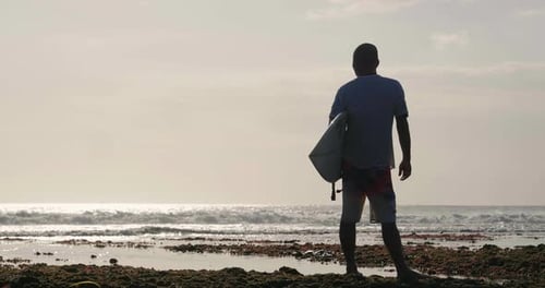 Silhouette bei Sonnenuntergang eines Surfers an der Küste mit Blick auf den Horizont, bevor er sich auf den Weg macht
