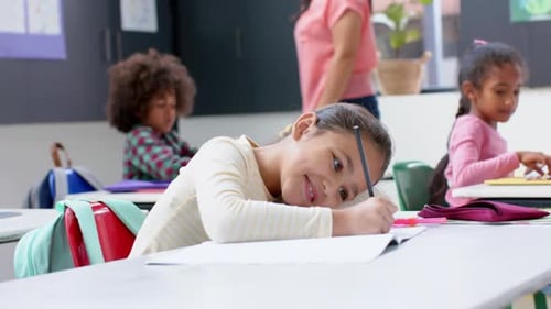 In school, girl smiling while writing in notebook at classroom desk