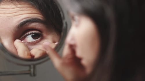 young woman looking at her face touching her eyes, refletcion in the mirror. close up of big brown e