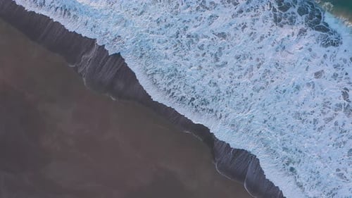 Diagonal drone footage of dynamic ocean waves coming ashore on sand beach
