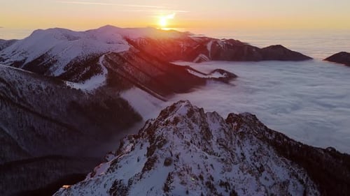 Aerial View of Sunset Over SnowCovered Rocky Peaks with Fog Blanketing the Valley Below