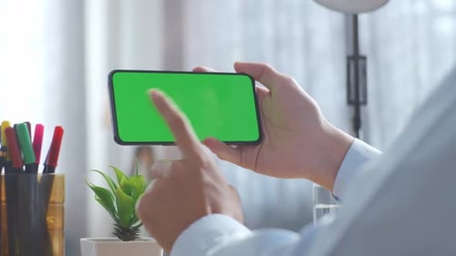 Close up of man's hands using a mock up green screen smartphone on a desk