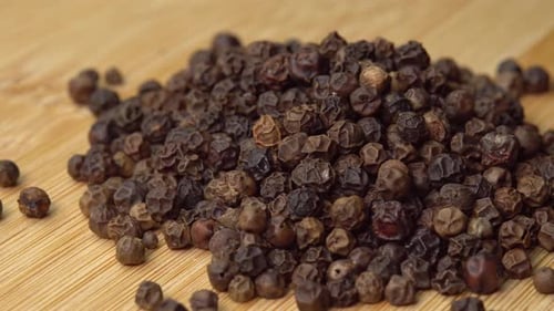 Pile of Whole Black Peppercorns on Wood Surface