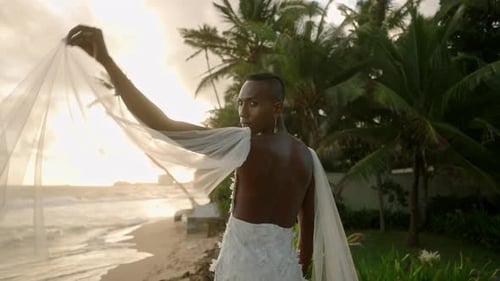 Flamboyant Gender Fluid Black Person Posing on Ocean Shore in White Chiffon Wedding Dress Nonbinary