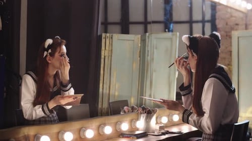 Woman Applying Makeup in Front of Illuminated Mirror