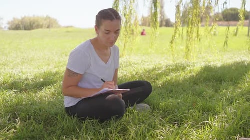 Woman with Pen Writing Sitting in Park Dressed White