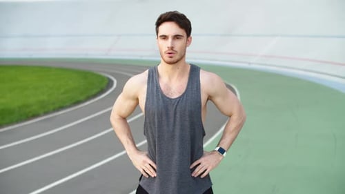 Muscular sport man squatting in sportswear during outdoor workout at stadium track