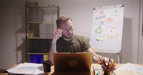 Exhausted Man Working with Laptop in Late Evening in Office