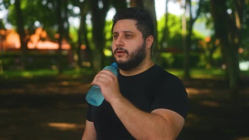 Young man drinking fresh water after running at the park being healthy and hydrated