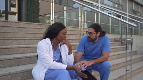 Video of male Doctor consoling his female colleague sitting on hospital steps