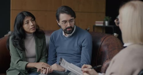 Female Psychologist Talking to Sad Young Couple Discussing Problems Doing Grief Counseling in Office