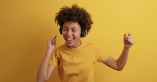 Upbeat millennial girl with afro hair jumps joyfully in yellow studio