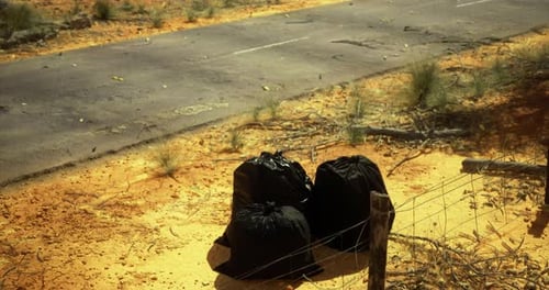 Black Garbage Bags Left on Roadside in Arid Landscape During Daylight