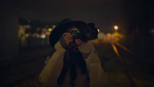 Woman Using Camera on Railroad Tracks at Night