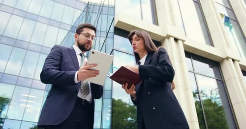Businessman and Businesswoman in Formal Suits Collaborating in Outdoor Near Modern Office Using
