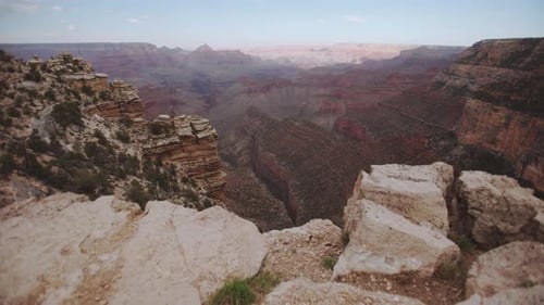 Grand Canyon cliff edge gimbal push forwards reveals valley below, with blue skies, cloud cover, sof